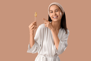 Canvas Print - Beautiful young happy woman pointing at spatula with sugaring paste on brown background