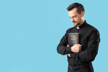 Portrait of male priest with holy Bible and prayer beads on blue background