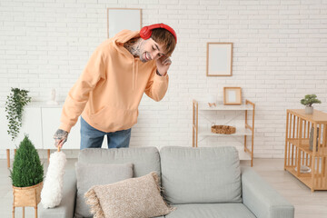 Wall Mural - Young tattooed man dancing with dust brush while cleaning his flat