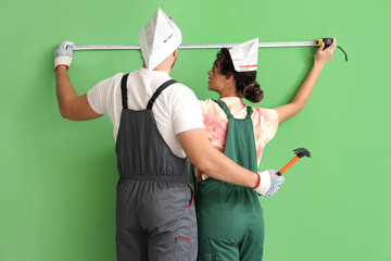 Poster - Beautiful young couple with measuring tape and hammer near green wall doing repair in new house