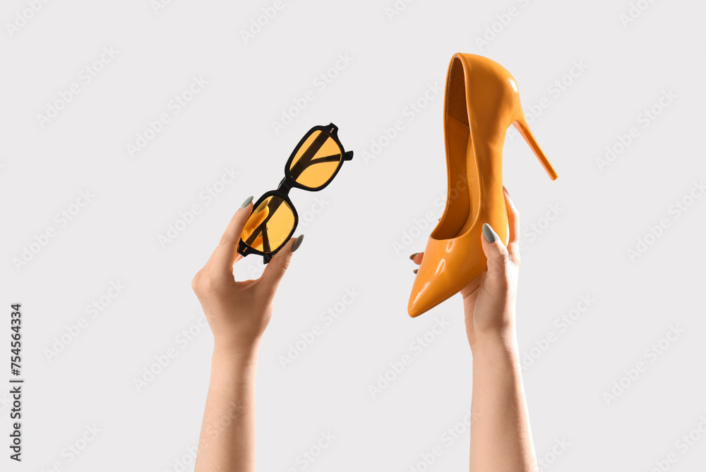 Female hands with stylish sunglasses and high heels on grey background