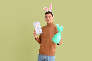 Wall Mural - Happy young man in bunny ears with gift box and surprise egg on green background. Easter celebration