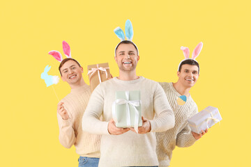 Wall Mural - Happy young men in bunny ears with gift boxes and paper decorations on yellow background. Easter celebration