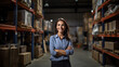 Confident woman is smiling and standing in a warehouse with shelves filled with boxes, suggesting a role in logistics or inventory management.