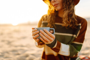 Young woman drinking morning coffee on the beach. Cup of coffee to keep warm. Travel, weekend, relax and lifestyle concept.