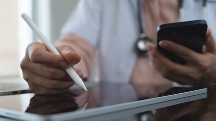 Wall Mural - Female doctor working, using digital tablet and mobile phone at doctor's office. writing prescription, recording patient's information, healthcare and medicine concept, close up