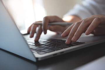 Wall Mural - closeup of woman hand typing, searching the information on laptop computer with a pen and notebook o