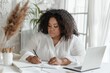 © evgenia_lo - Plus-size young woman concentrating on writing, with a laptop on her desk.