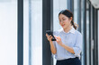 © SOMKID - Asian businesswoman using smartphone standing at the office.