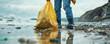 A person is walking on a beach with a yellow bag, picking up trash. Concept of responsibility and care for the environment, as the person is actively working to clean up the beach