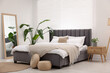 Stylish bedroom interior with large bed, mirror and houseplants