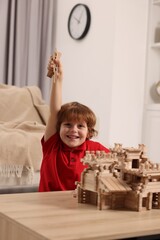 Poster - Emotional boy playing with wooden castle at table in room. Child's toy