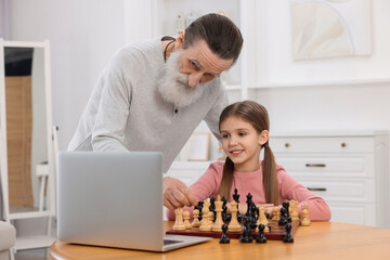 Wall Mural - Grandfather teaching his granddaughter to play chess following online lesson at home