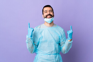 Wall Mural - Surgeon man with beard with blue uniform over isolated purple background pointing up a great idea