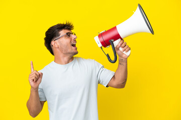 Sticker - Young caucasian handsome man isolated on yellow background shouting through a megaphone to announce something in lateral position