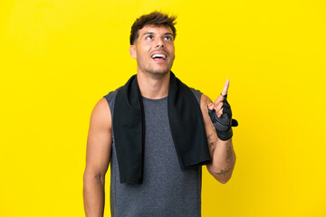 Wall Mural - Young sport caucasian man with towel isolated on yellow background pointing up and surprised