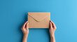 © Hasanka - Woman holding kraft paper envelope on light blue background, closeup, person holding envelope