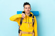 Young mountaineer man with a big backpack over isolated blue background showing thumb down sign