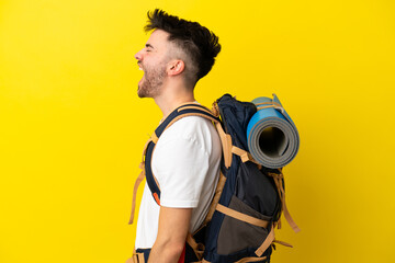 Wall Mural - Young mountaineer caucasian man with a big backpack isolated on yellow background laughing in lateral position