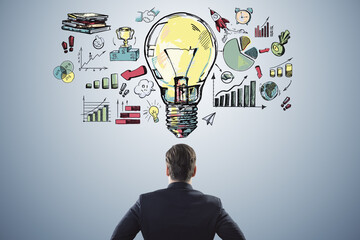 Wall Mural - Back view of young male in suit looking at creative business sketch with huge light bulb and other icons. Idea, innovation and financial growth concept.