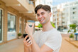 Young handsome man using mobile phone and holding a coffee with happy expression