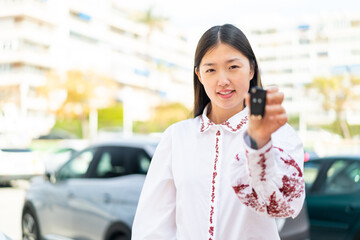 Wall Mural - Young Chinese woman holding car keys at outdoors with happy expression