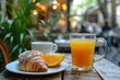 Classic French morning meal at a bistro patio with chocolate croissant, open-faced sandwich, and fresh orange juice.