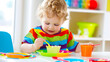 A toddler in a colorful outfit intently focused on eating a healthy snack from a bright bowl at a child-sized table.
