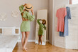 © mary_markevich - young pretty woman in green dress trying on style trend dress looking in mirror