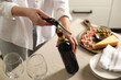 Woman opening wine bottle with corkscrew at table indoors, closeup