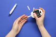 Diabetes. Woman checking blood sugar level with glucometer on blue background, top view