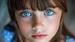 © imagineRbc - A young girl with blue eyes and freckles stares at the camera. Concept of innocence and curiosity, as the girl's gaze seems to be searching for something or someone