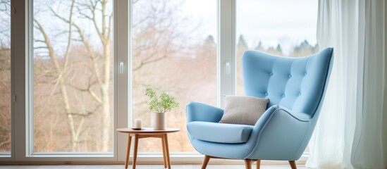 Poster - A wooden chair is placed in front of a window in the living room of a house, overlooking a green plant on the floor. The fixture adds a touch of blue to the rooms decor