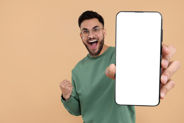 happy man holding smartphone with empty screen on beige background, space for text