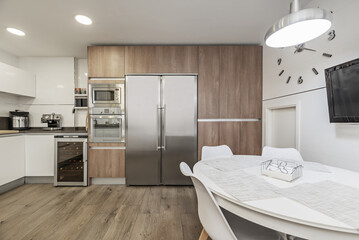 Wall Mural - Image of a furnished kitchen in a single-family home with integrated stainless steel appliances covering a wall with light wood furniture