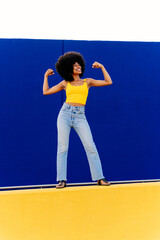 Wall Mural - Beautiful young black woman with curly afrp hair style and colorful clothing strolling  outdoors in the city