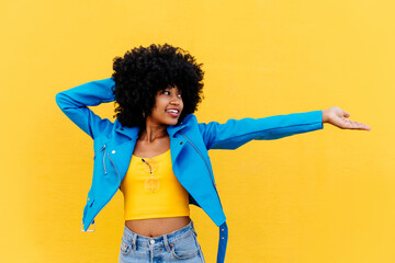 Wall Mural - Beautiful young black woman with curly afrp hair style and colorful clothing strolling  outdoors in the city