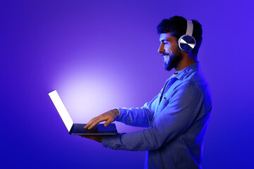 Poster - Bearded guy with earphones stands typing on laptop, neon background