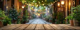 Fototapeta  - Rustic wooden tabletop with a dreamy blurred background of glowing string lights and green foliage, evoking a cozy evening ambiance.