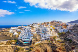 Fototapeta Tulipany - Aerial drone view of famous Oia village with white houses and blue dome churches on Santorini island, Aegean sea, Greece.