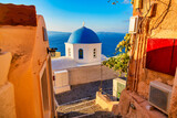 Fototapeta Tulipany - Oia village Image. Blue church and narrow street with yellow houses on Santorini island, Greece