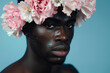 A man of African descent adorns a splendid floral crown against a backdrop of soft pastel blue, emphasizing men's well-being and skincare.