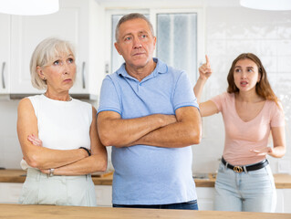 Wall Mural - Adult daughter scolds elderly parents, mom and dad, in a modern kitchen