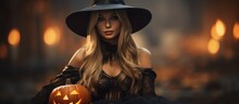 A Beautiful Young Woman Dressed In A Witch Costume And Hat Holds A Carved Pumpkin In Her Hands.