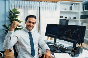 Successful in trader businessman looking at camera with two stock exchange investment screens, raising fist up to earn high profit, dynamic financial technology graph stock market at office. Surmise.