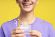 Happy boy with braces holding different interdental brushes, flossing isolated on yellow background