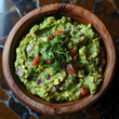 A wooden bowl filled with guacamole, made with avocados, lime, cilantro, and seasonings, sits on a table as a delicious dish made from fresh produce and leafy vegetables