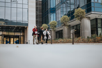 Three professional business people engaged in a conversation while walking outside a modern office building.