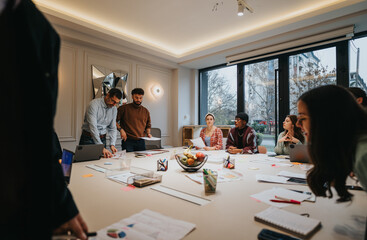 Poster - A multicultural team collaborates around a table filled with laptops and notes in a well-lit, contemporary office setting.