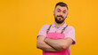 Portrait of handsome mechanic with stubble in pink overall, shirt having his arms crossed, looking at camera, isolated on yellow background professional photography